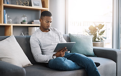 Buy stock photo Remote work, tablet and man on sofa reading email, social media post or streaming video on subscription service. Search, scroll and internet, freelance worker checking website on couch in living room