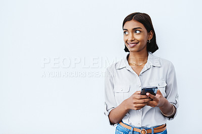 Buy stock photo Social media, young Indian woman on smartphone and thinking in studio background. Smiling or idea, phone for communication or networking and happy female person standing with cellphone in backdrop
