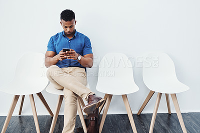 Buy stock photo Full length studio shot of a young businessman sitting down on a chair and using his cellphone