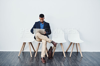 Buy stock photo Full length studio shot of a young businessman sitting down on a chair and using his laptop