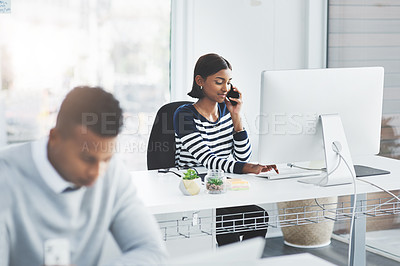 Buy stock photo Shot of a young businesswoman taking a phone call at her office desk with a colleague working in the foreground