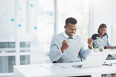 Buy stock photo Shot of a young businessman celebrating at his office desk with a colleague working in the background