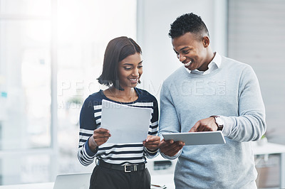 Buy stock photo Shot of two young businesspeople standing in their office and working together using a digital tablet
