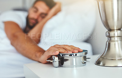 Buy stock photo Cropped shot of a tired young man sleeping in his bed while turning off the alarm clock
