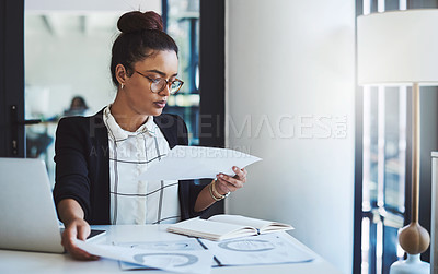 Buy stock photo Shot of a young businesswoman going through paperwork at her desk in a modern office