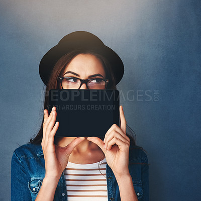 Buy stock photo Shot of an attractive young woman holding tablet in front of her face in studio