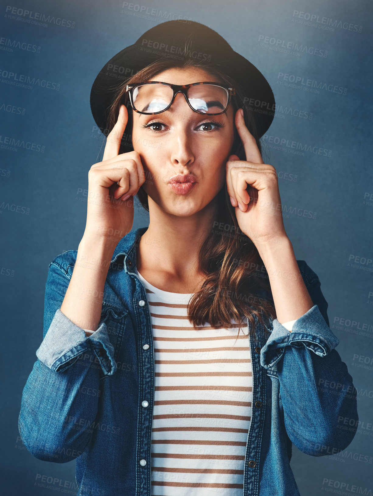Buy stock photo Studio shot of an attractive young woman lifting her glasses and pouting against a blue background