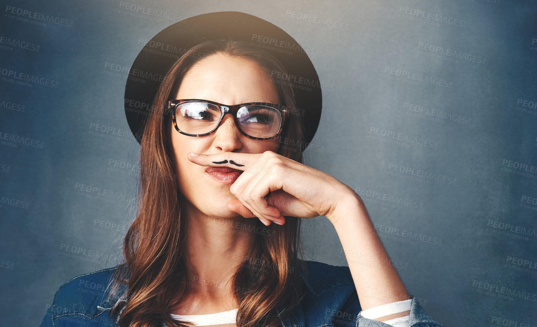 Buy stock photo Young woman, thinking and hat with finger mustache or grumpy attitude in studio on a gray background. Female person, hipster or comedian in wonder with secret identity, nerdy impression or fake hair