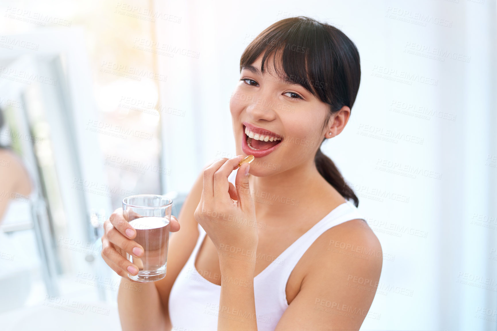 Buy stock photo Portrait of a cheerful attractive young woman taking medication at home during the day