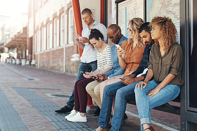 Buy stock photo Shot of a group of people using their cellphones while sitting at a bus stop in the city