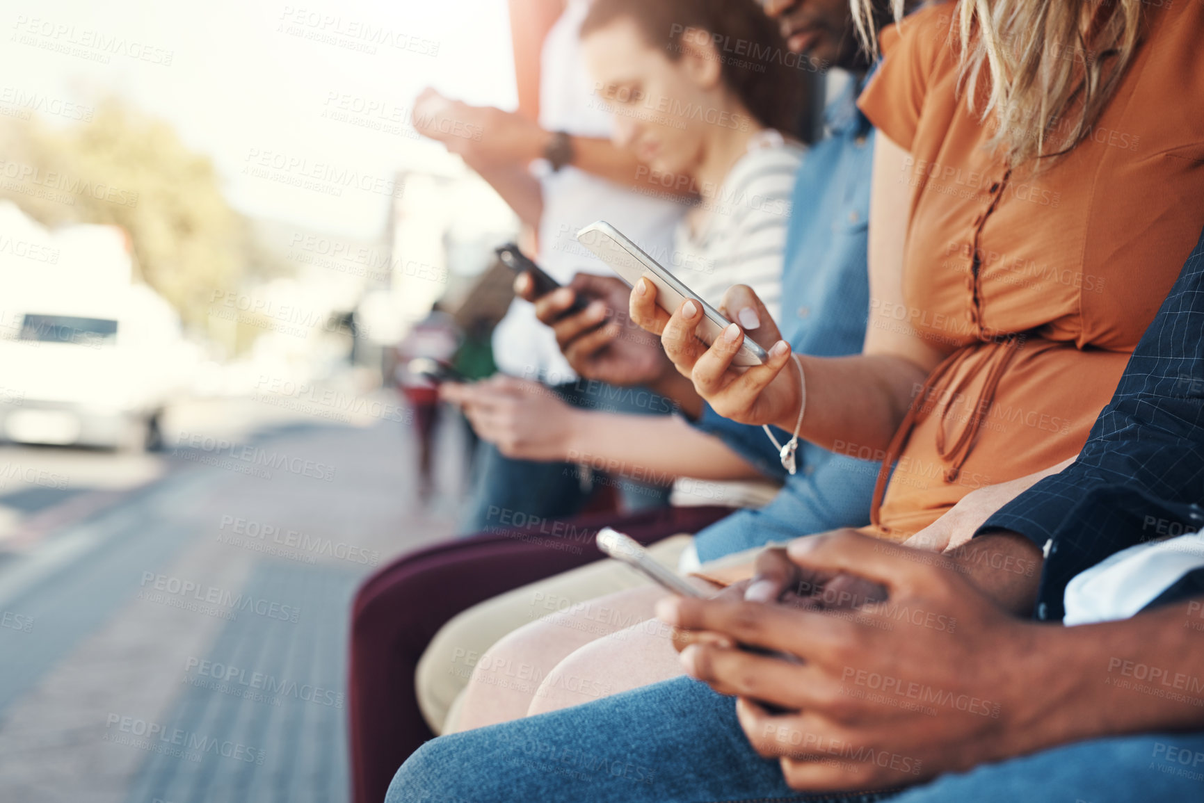 Buy stock photo Closeup shot of a group of people using their cellphones while sitting at a bus stop in the city