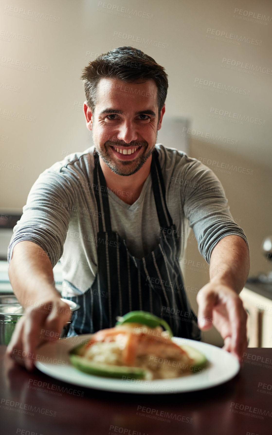 Buy stock photo Cropped portrait of a handsome young man serving food in the kitchen at home
