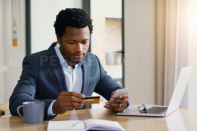 Buy stock photo Shot of a handsome young businessman holding a credit card and a cellphone at home