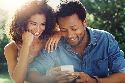 Buy stock photo Shot of an affectionate young couple using a cellphone together while relaxing outdoors