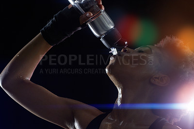 Buy stock photo Studio shot of a young sportswoman drinking from a water bottle against a dark background