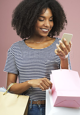 Buy stock photo Studio shot of a beautiful young woman using her cellphone while carrying shopping bags