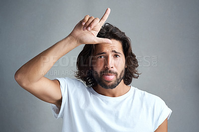 Buy stock photo Studio portrait of a young man showing a loser gesture against a grey background