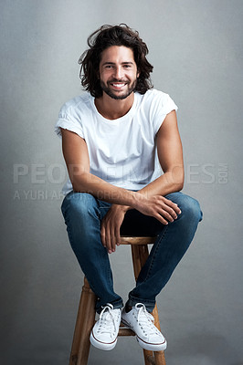 Buy stock photo Fashion, smile and portrait of man in studio on a stool with casual, cool and stylish outfit. Happy, handsome and confident young male model from Mexico with trendy style on chair by gray background.