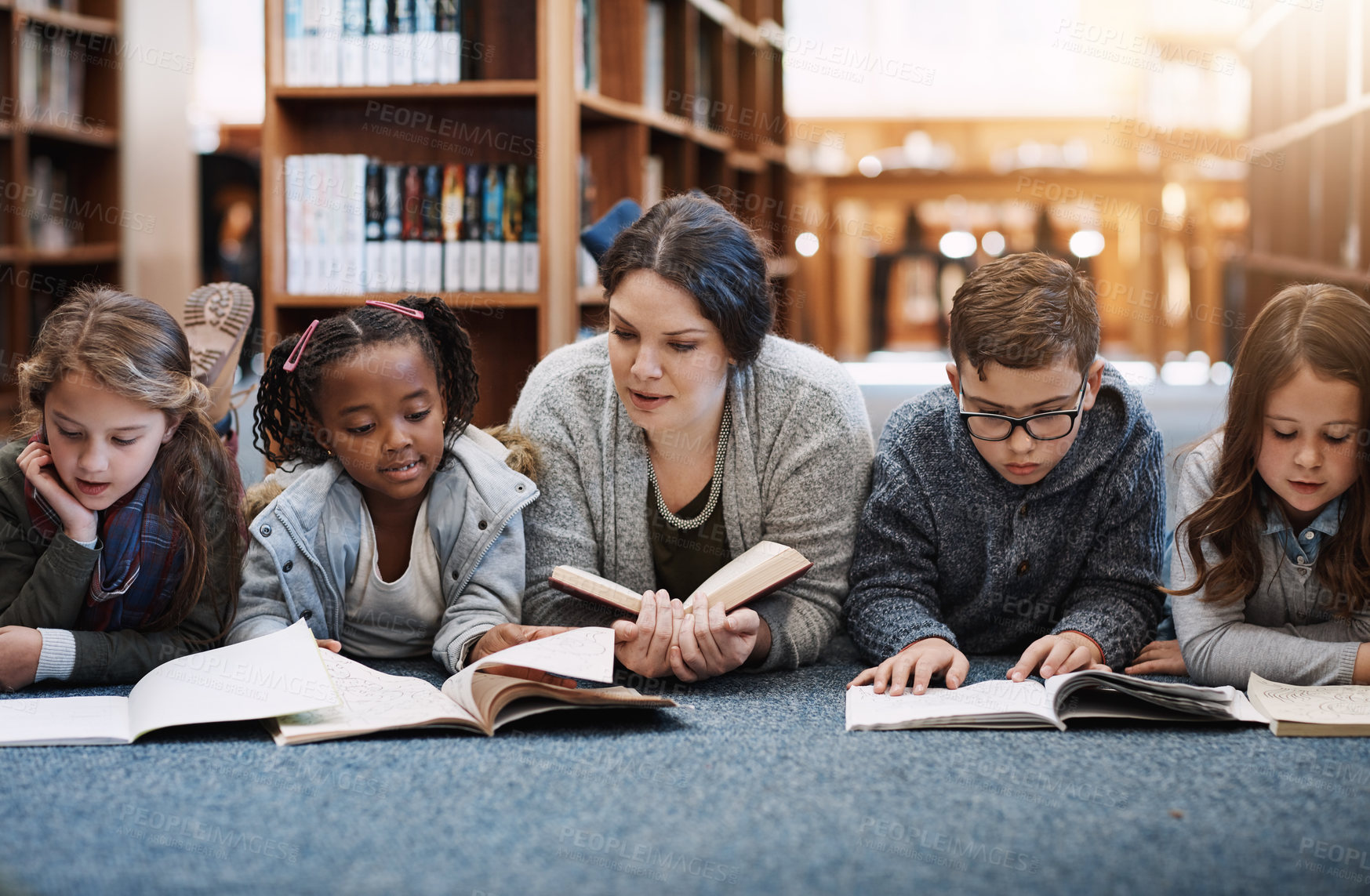 Buy stock photo Cropped shot of elementary school kids reading with their teacher on the floor in the library