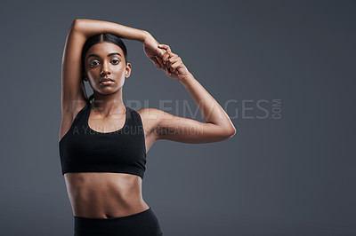 Buy stock photo Portrait, mockup and stretch with a sporty woman in studio on a gray background for fitness or health. Exercise, workout and warm up with a young focused indian female athlete training her body