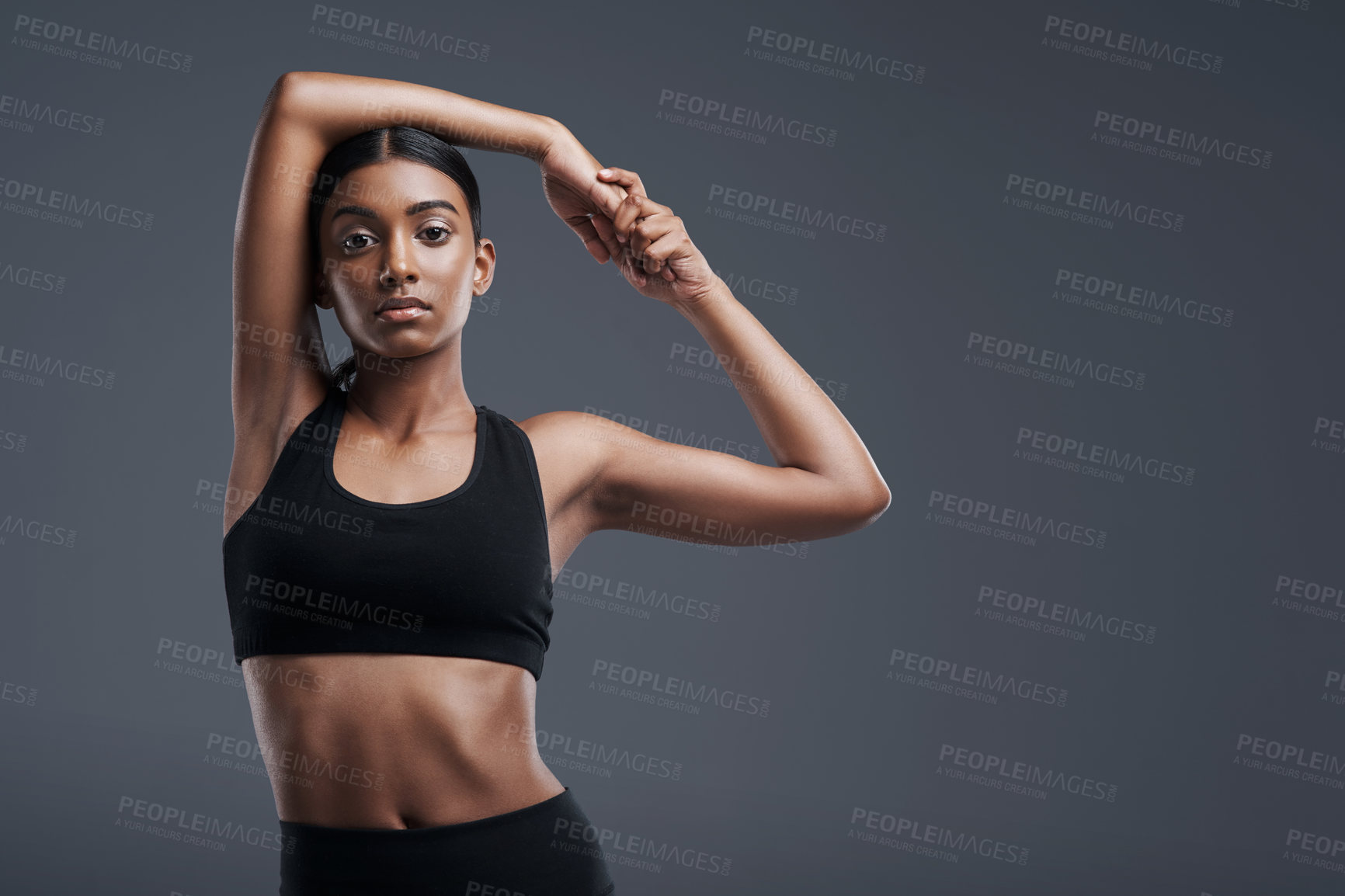 Buy stock photo Portrait, mockup and stretch with a sporty woman in studio on a gray background for fitness or health. Exercise, workout and warm up with a young focused indian female athlete training her body