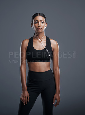 Buy stock photo Studio portrait of a sporty young woman listening to music against a grey background