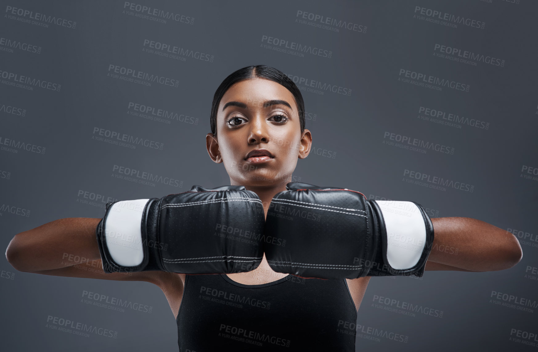 Buy stock photo Studio portrait of a sporty young woman wearing boxing gloves against a grey background