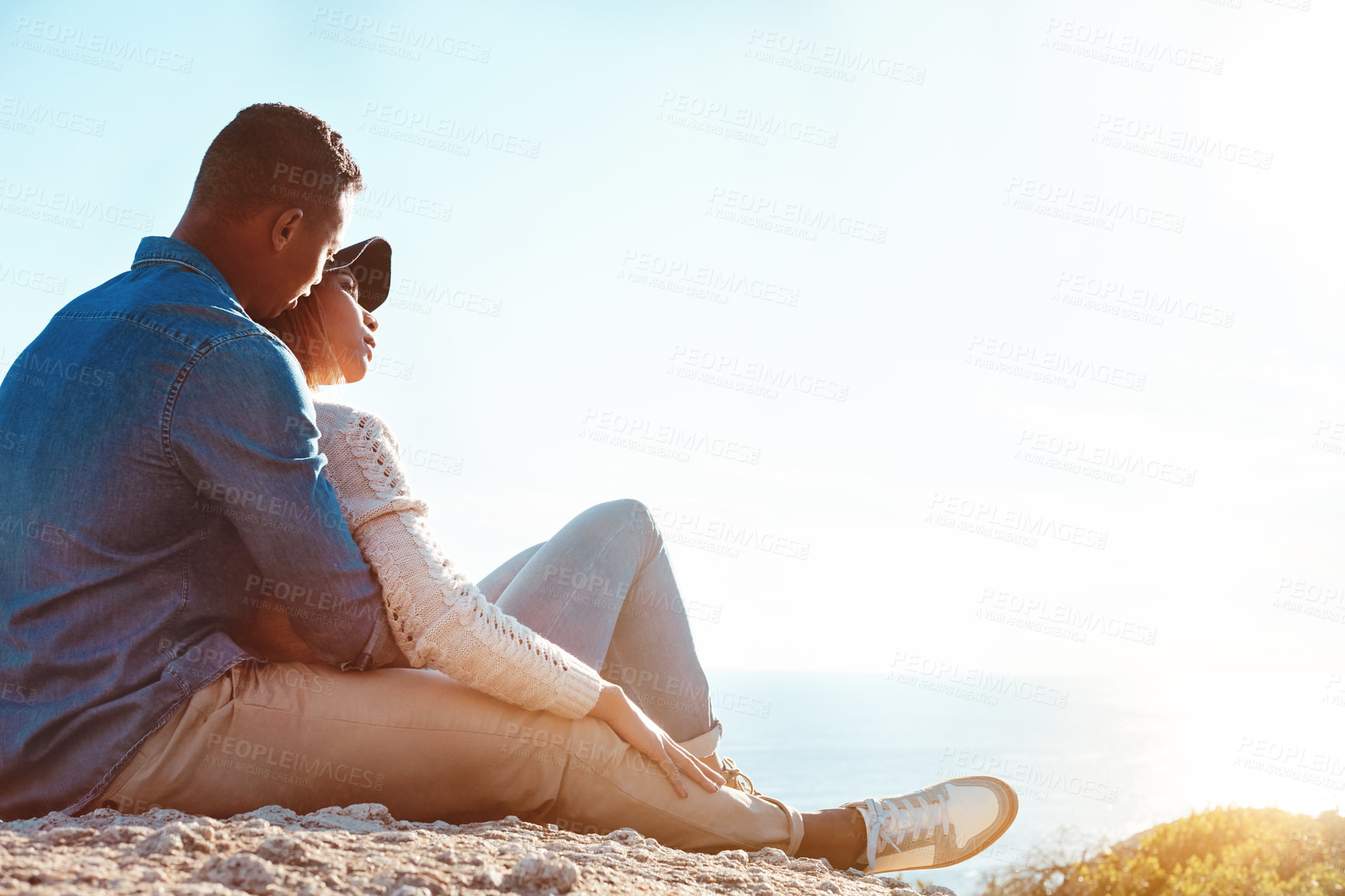 Buy stock photo Shot of a happy young couple sitting on a rock and enjoying the ocean view