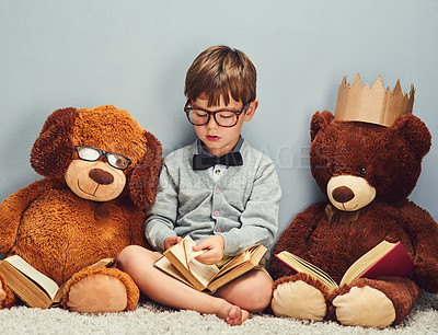 Buy stock photo Studio shot of a smart little boy reading a book next to his teddy bears against a gray background