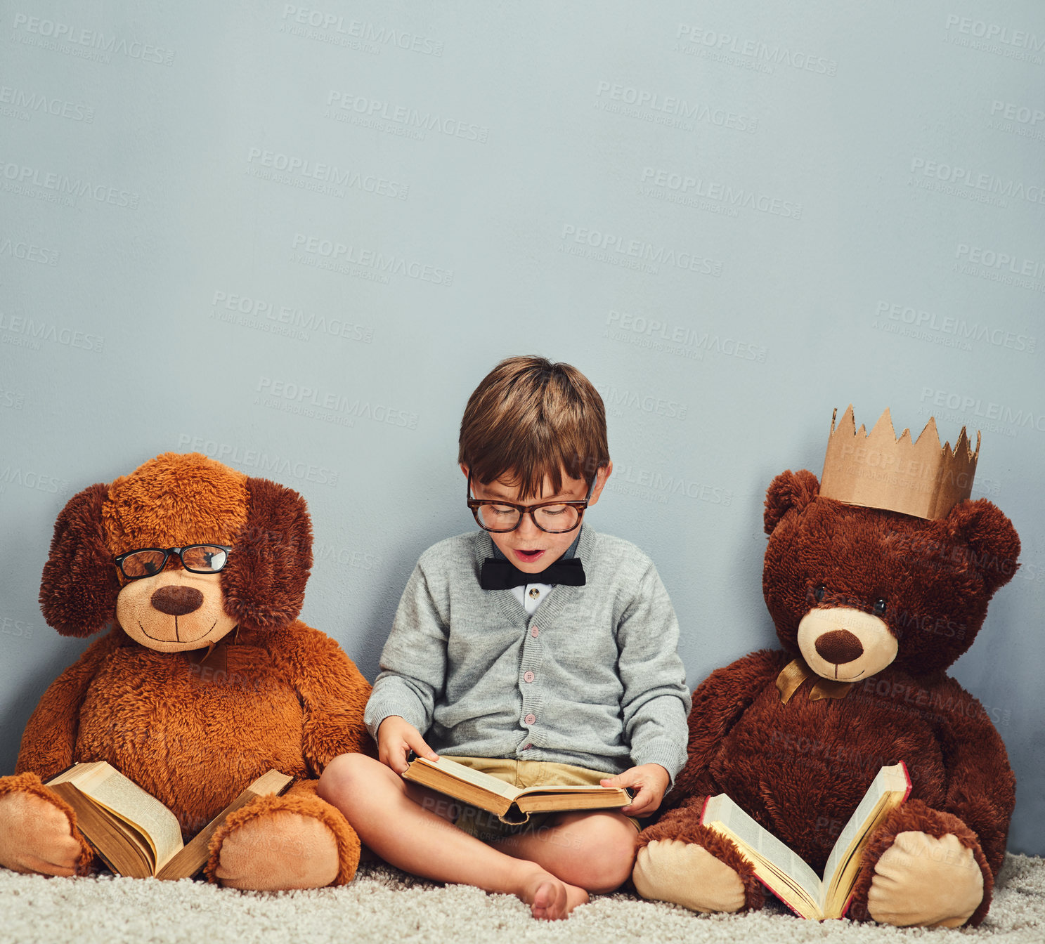 Buy stock photo Studio shot of a smart little boy reading a book next to his teddy bears against a gray background