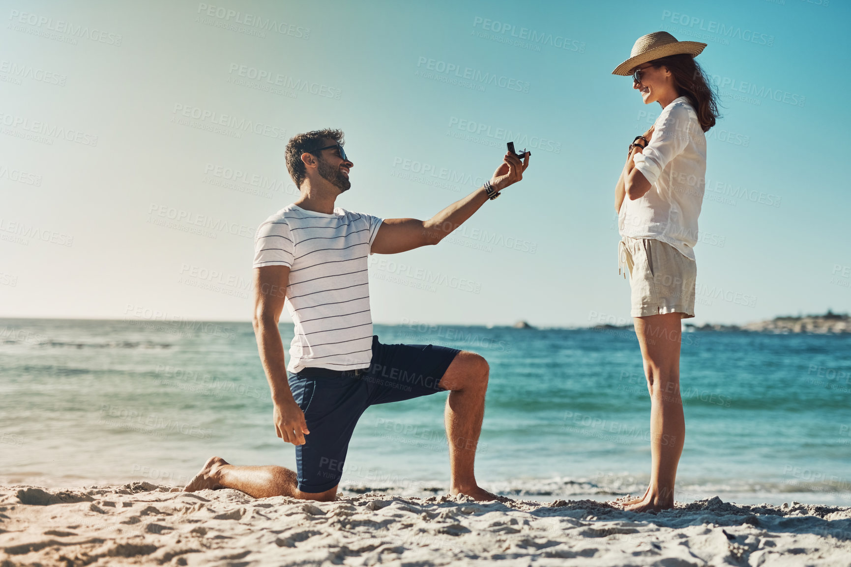 Buy stock photo Full length shot of a young man proposing to his girlfriend at the beach on a summer’s day