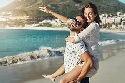 Buy stock photo Cropped portrait of a handsome young man giving his girlfriend a piggyback ride at the beach