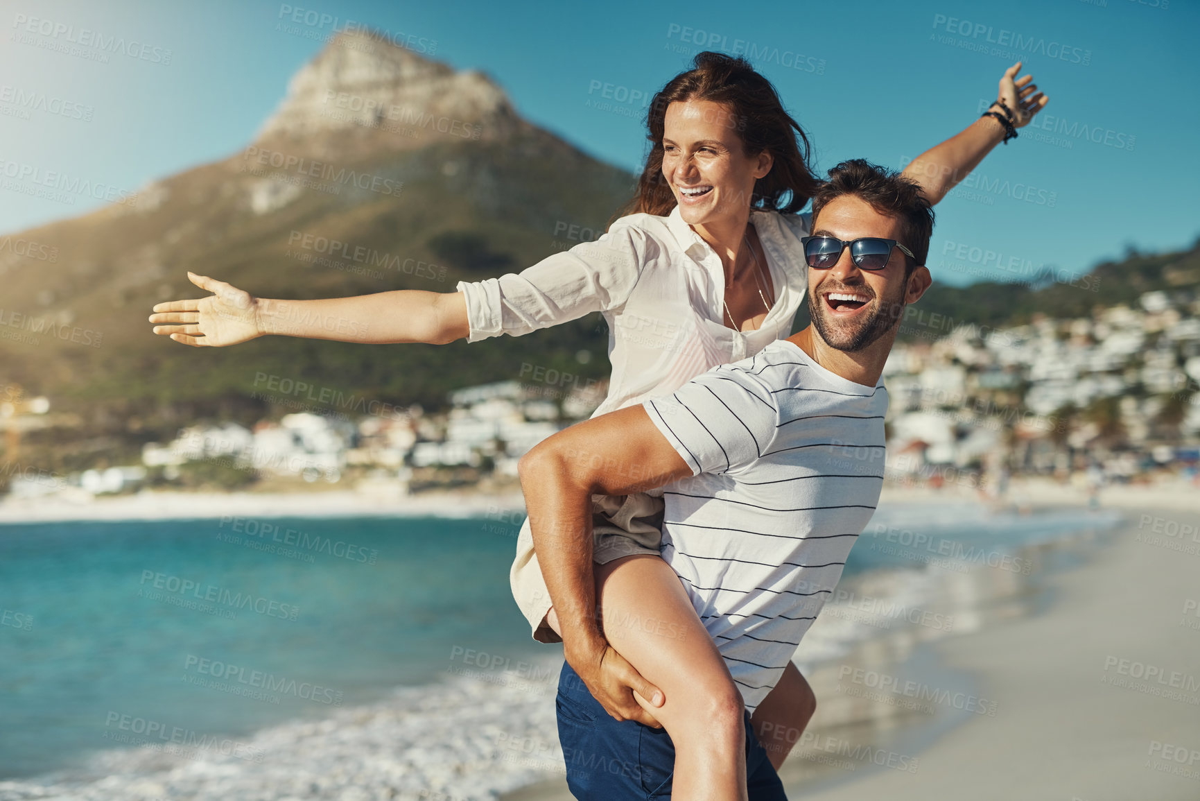 Buy stock photo Cropped shot of a handsome young man giving his girlfriend a piggyback ride at the beach