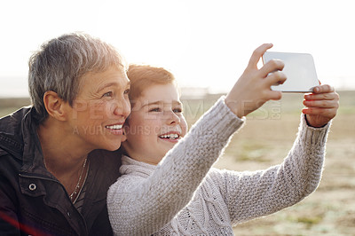 Buy stock photo Shot of an adorable little boy taking a selfie with his grandmother outdoors