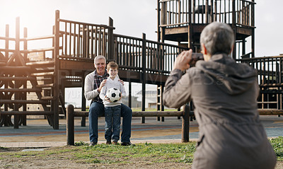 Buy stock photo Rearview shot of a grandmother taking a picture of her husband and grandson posing together outdoors