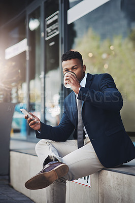 Buy stock photo Shot of a handsome young businessman using a cellphone while drinking coffee in the city