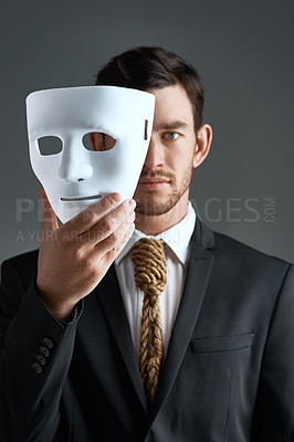 Buy stock photo Studio portrait of a young businessman holding a mask in front of his face against a gray background