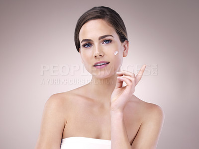 Buy stock photo Studio portrait of a young woman applying moisturizer to her face against a pink background
