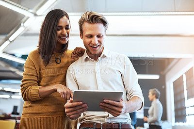 Buy stock photo Cropped shot of two young businesspeople looking at a tablet in their office