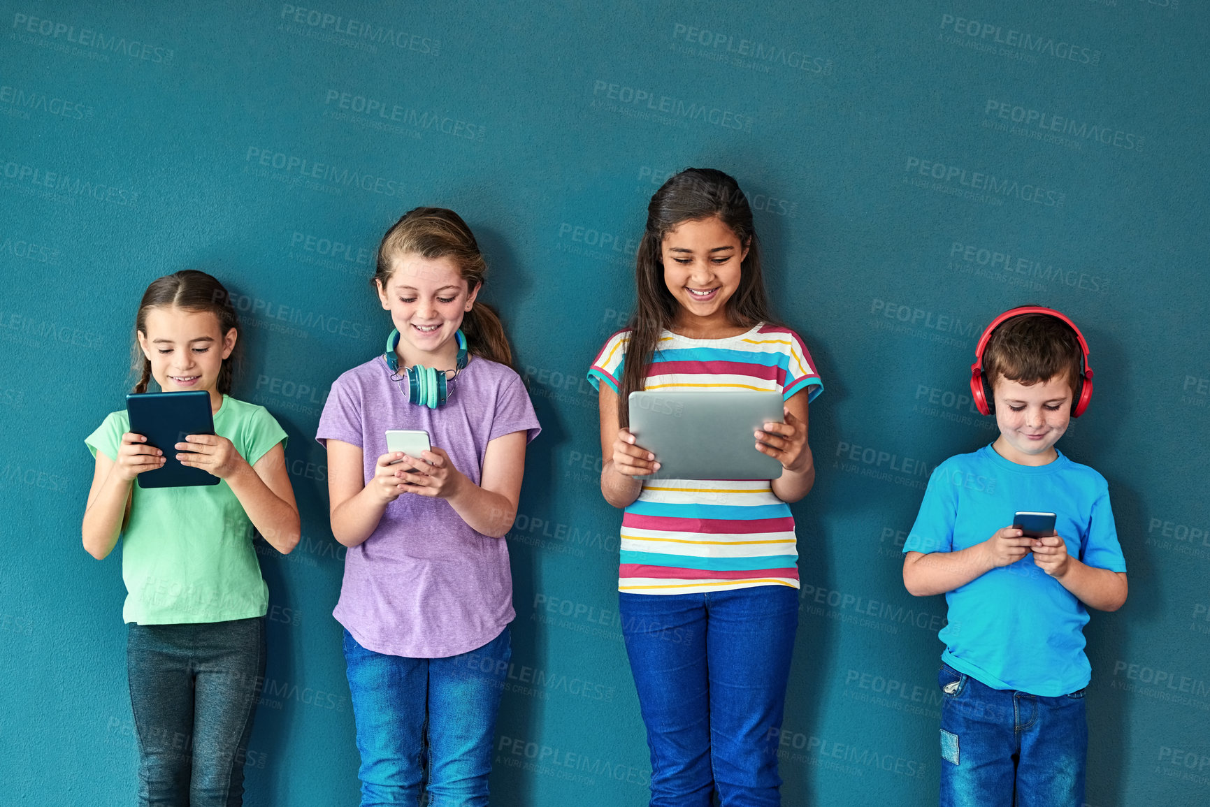 Buy stock photo Studio, technology and group of kids for elearning, education and online research with smile. Happy students, girls and boy with digital app of tablet, smartphone and headphone by blue background