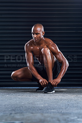 Buy stock photo Shot of a sporty young man tying his shoelaces in the middle of his exercise routine