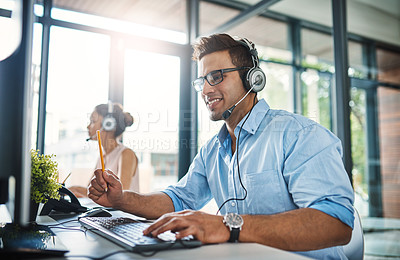 Buy stock photo Cropped shot of a handsome young man working in a call center with a female colleague in the background