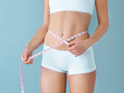 Buy stock photo Studio shot of a healthy woman measuring her waistline with a tape measure against a purple background
