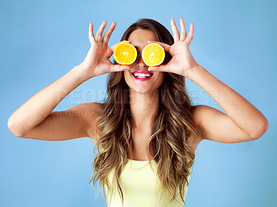 Buy stock photo Studio shot of a young woman covering her eyes with oranges against a blue background
