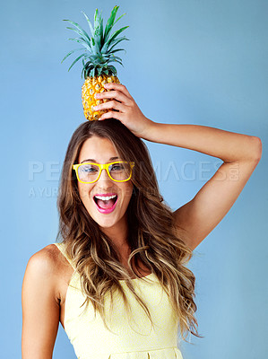 Buy stock photo Studio shot of a young woman balancing a pineapple on her head against a blue background