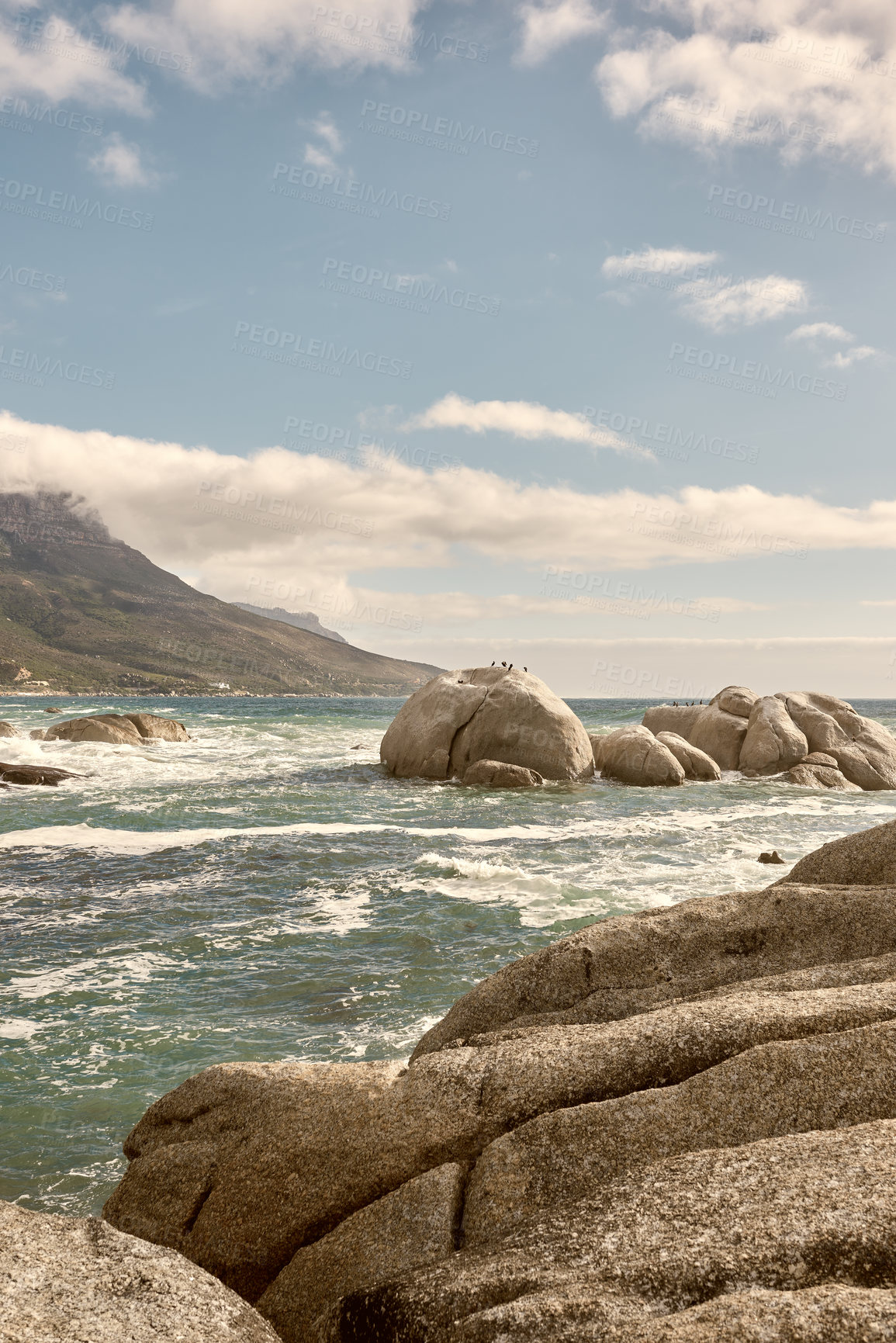Buy stock photo Rocks in the ocean under a blue cloudy sky with copy space. Scenic landscape of beach waves splashing against boulders or big stones in the sea at a popular summer location in Cape Town, South Africa