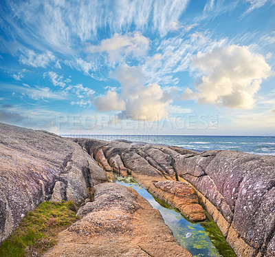 Buy stock photo Ocean view on a shallow rocky shoreline with Lion's Head, Table Mountain National Park in Cape Town, South Africa in the background. Quiet calm beach during sunset on a beautiful summer day