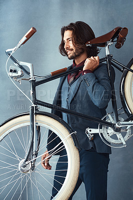 Buy stock photo Studio shot of a stylishly dressed handsome young man carrying his bicycle against a gray background