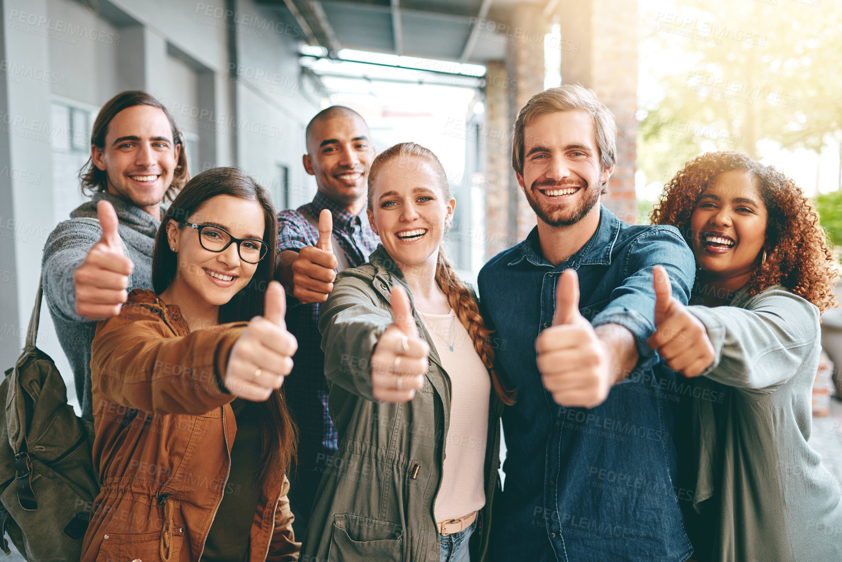 Buy stock photo Portrait of a group of happy young students giving thumbs up together on campus
