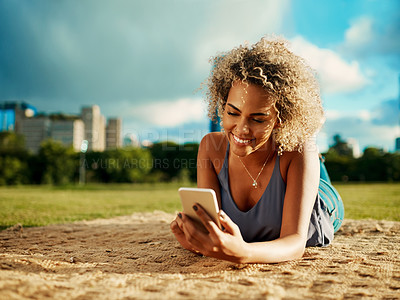 Buy stock photo Cropped shot of an attractive young woman using a smartphone while lying down at a park